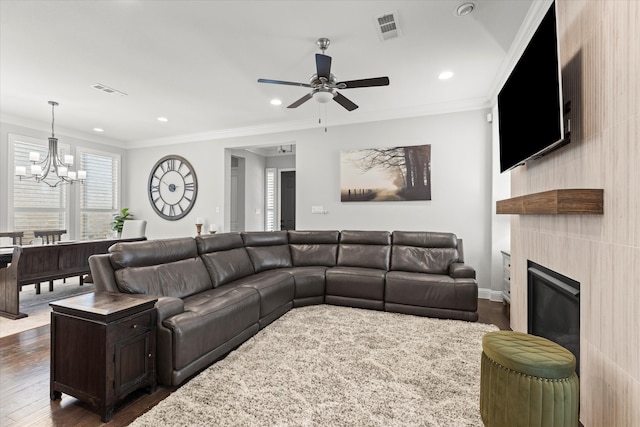 living area featuring dark wood-type flooring, ceiling fan with notable chandelier, visible vents, and ornamental molding