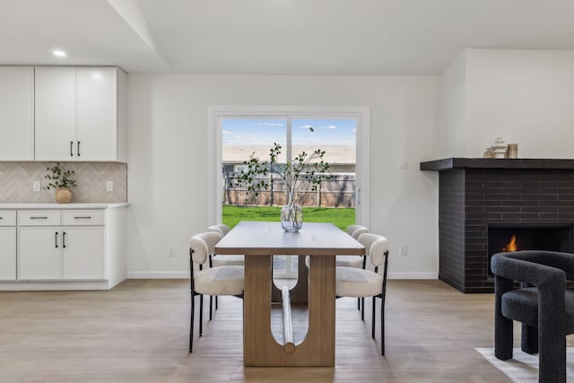 dining space with a brick fireplace, baseboards, and light wood-type flooring