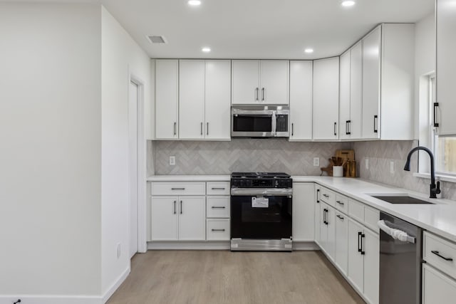 kitchen featuring light countertops, light wood-style flooring, stainless steel appliances, white cabinetry, and a sink