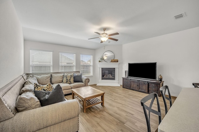 living room featuring baseboards, visible vents, light wood finished floors, ceiling fan, and a glass covered fireplace