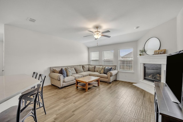 living area with light wood finished floors, visible vents, baseboards, ceiling fan, and a glass covered fireplace