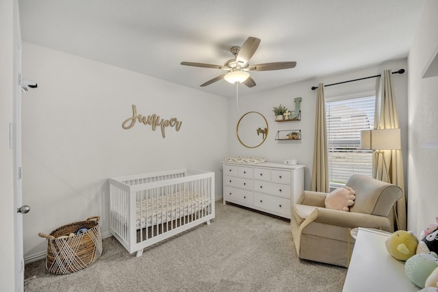 carpeted bedroom with a crib and ceiling fan