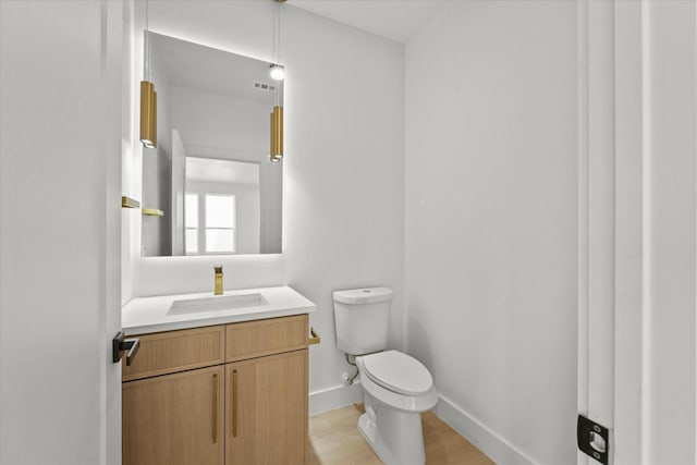 bathroom featuring baseboards, toilet, wood finished floors, and vanity