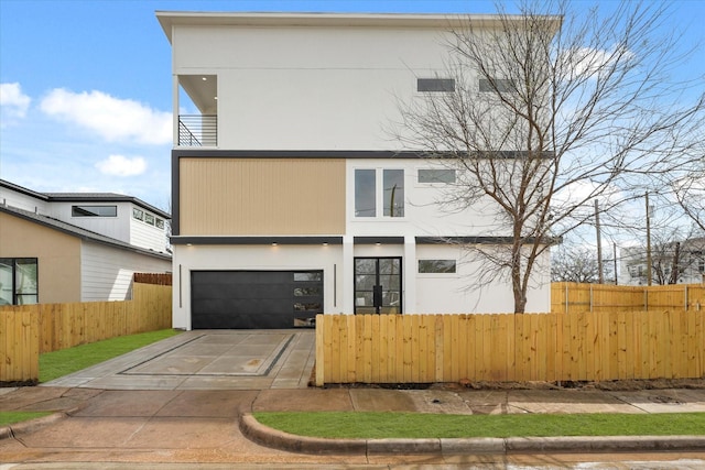 contemporary house with stucco siding, an attached garage, driveway, and fence