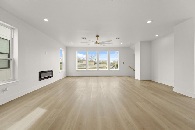 unfurnished living room with a glass covered fireplace, light wood-style flooring, recessed lighting, and baseboards