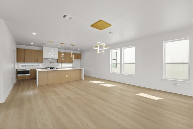 kitchen with visible vents, baseboards, open floor plan, light wood-type flooring, and light countertops