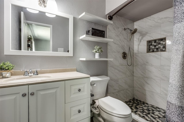 bathroom with tiled shower, toilet, vanity, and a textured wall