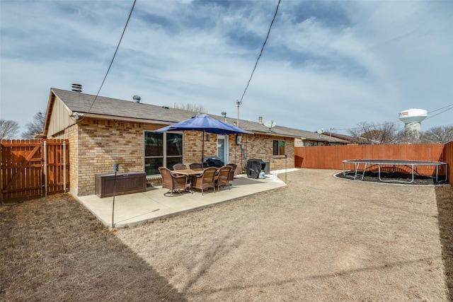 back of house featuring brick siding, a patio, a trampoline, and fence