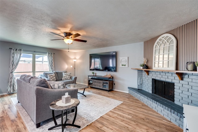 living room with wood finished floors, baseboards, a fireplace, ceiling fan, and a textured ceiling