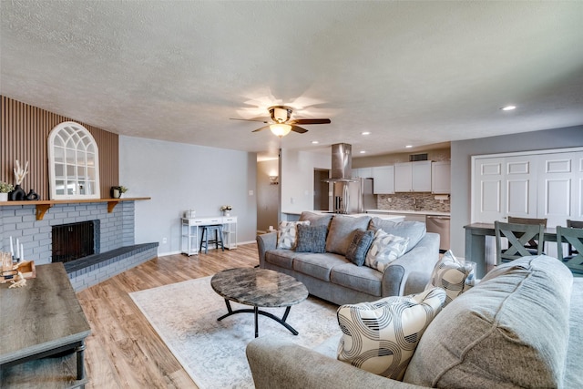 living area with visible vents, baseboards, light wood-style floors, a textured ceiling, and a ceiling fan