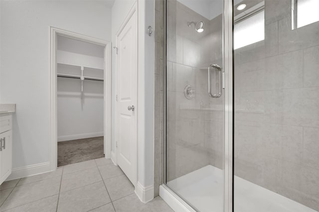 bathroom with vanity, baseboards, a stall shower, a walk in closet, and tile patterned floors