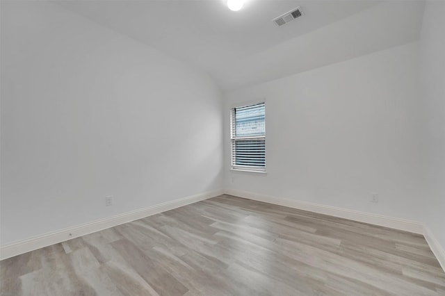 spare room featuring visible vents, baseboards, light wood-style floors, and vaulted ceiling