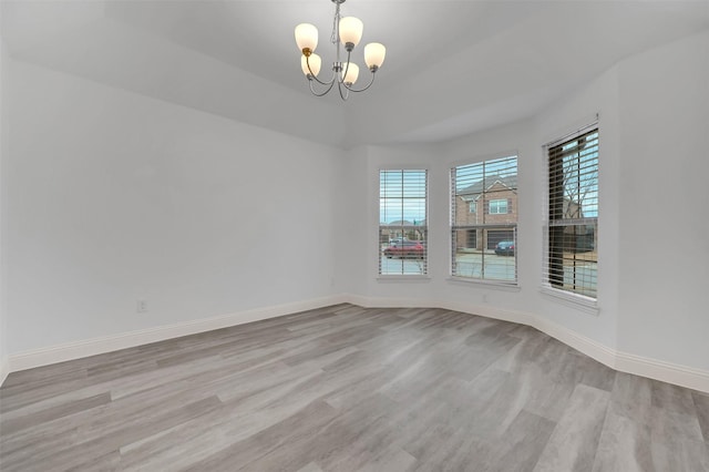 empty room with a notable chandelier, light wood-style floors, and baseboards