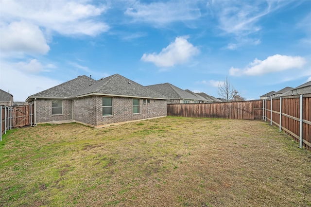 back of property featuring brick siding, a lawn, a shingled roof, and a fenced backyard