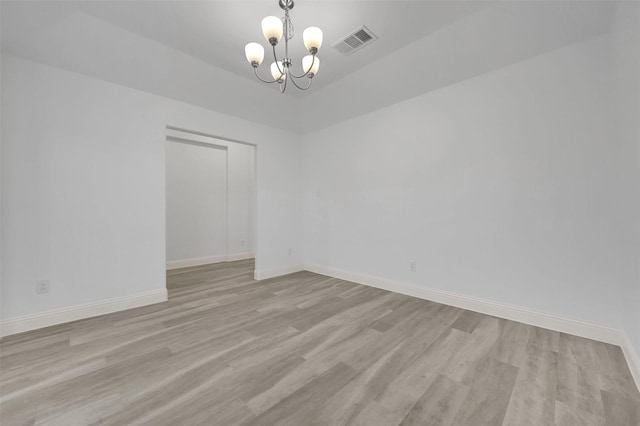 unfurnished room with an inviting chandelier, wood finished floors, visible vents, and baseboards