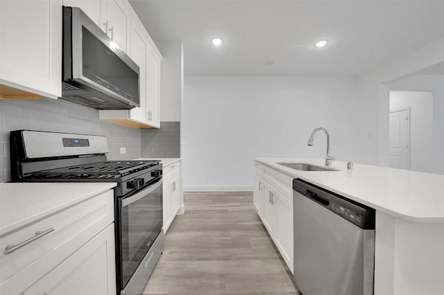 kitchen with a sink, backsplash, stainless steel appliances, light wood-style floors, and light countertops