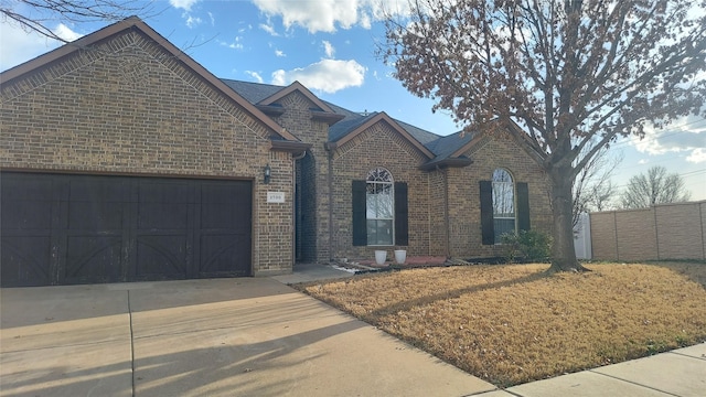 view of front facade with brick siding, an attached garage, concrete driveway, and fence