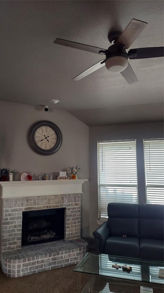 living area with lofted ceiling, a textured ceiling, a brick fireplace, and ceiling fan