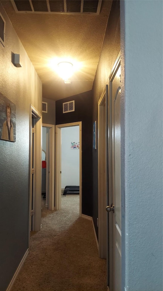 hallway with visible vents, carpet, and a textured wall