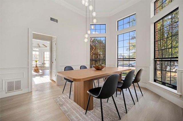 dining space with light wood-type flooring, visible vents, a wainscoted wall, and crown molding