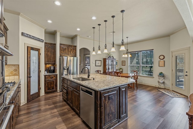 kitchen featuring an island with sink, a sink, stainless steel appliances, arched walkways, and decorative backsplash