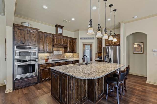 kitchen featuring a center island with sink, a sink, tasteful backsplash, stainless steel appliances, and dark brown cabinets