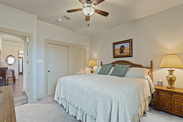 bedroom with visible vents, a ceiling fan, a closet, arched walkways, and light colored carpet