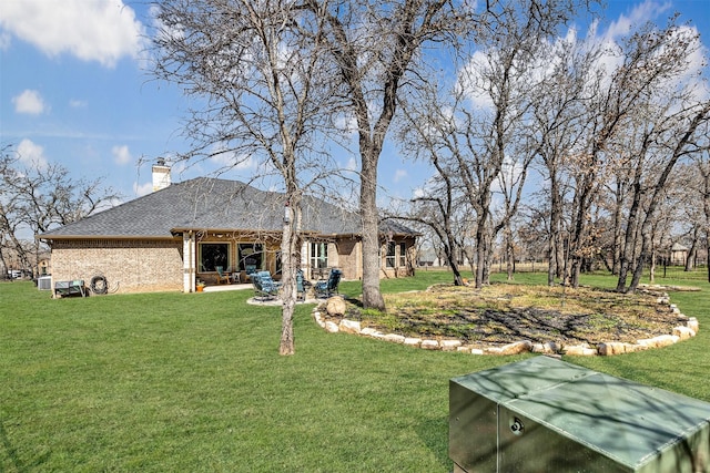 rear view of house with brick siding, roof with shingles, a lawn, a chimney, and a patio