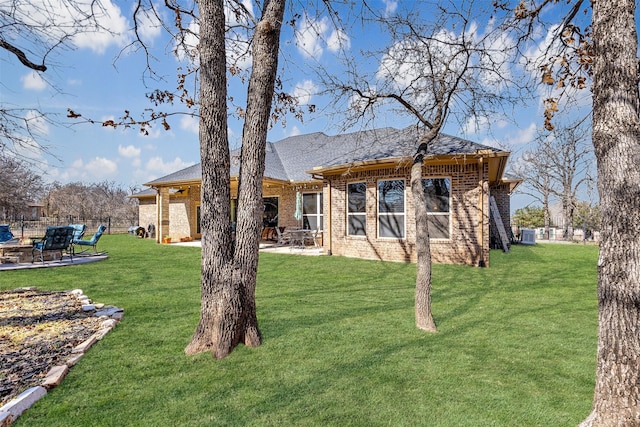 back of property featuring fence, a yard, a shingled roof, a patio area, and brick siding