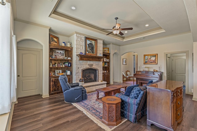 living area featuring a tray ceiling, dark wood-style floors, arched walkways, and ceiling fan