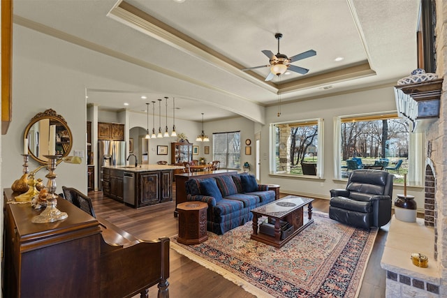 living room with arched walkways, a raised ceiling, ceiling fan, and dark wood-style flooring