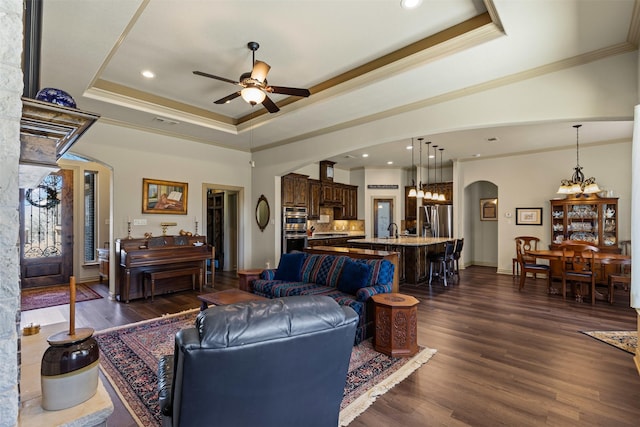 living room featuring arched walkways, a raised ceiling, and dark wood finished floors