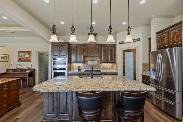 kitchen featuring dark brown cabinetry, light stone counters, appliances with stainless steel finishes, and a sink