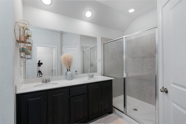 bathroom with a sink, double vanity, a shower stall, and vaulted ceiling