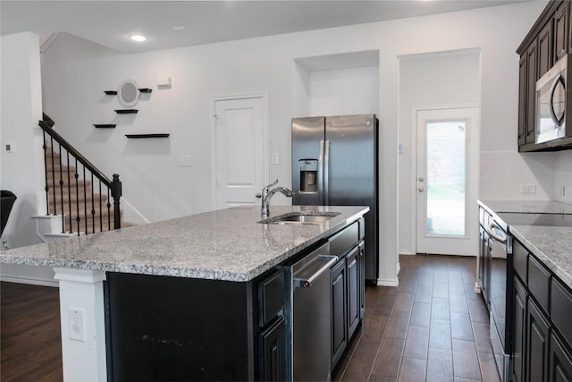 kitchen with a center island with sink, a sink, tasteful backsplash, dark wood-style floors, and stainless steel appliances