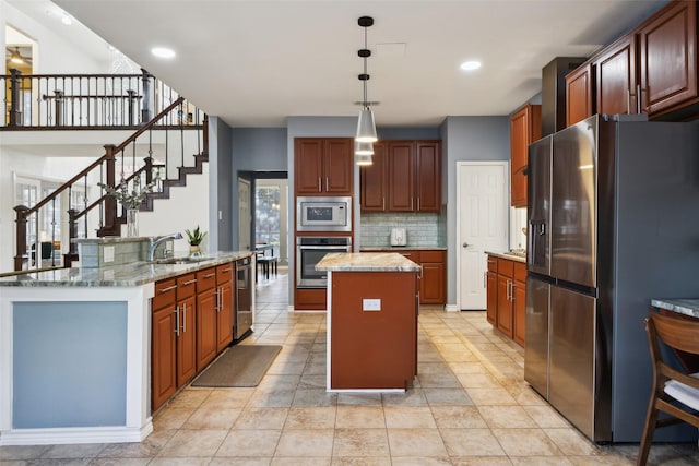 kitchen featuring a kitchen island with sink, a sink, stainless steel appliances, decorative light fixtures, and tasteful backsplash