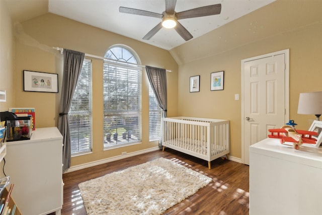 bedroom with baseboards, wood finished floors, a nursery area, and vaulted ceiling