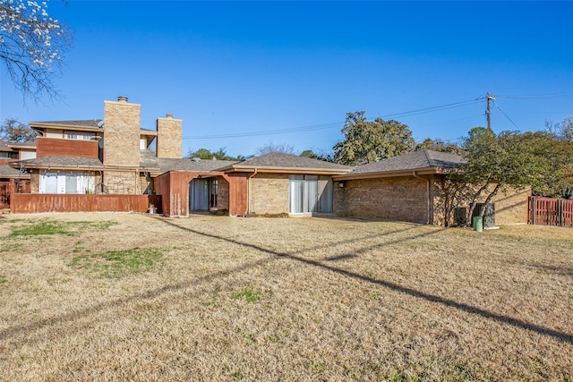 rear view of house with a yard, brick siding, a chimney, and fence