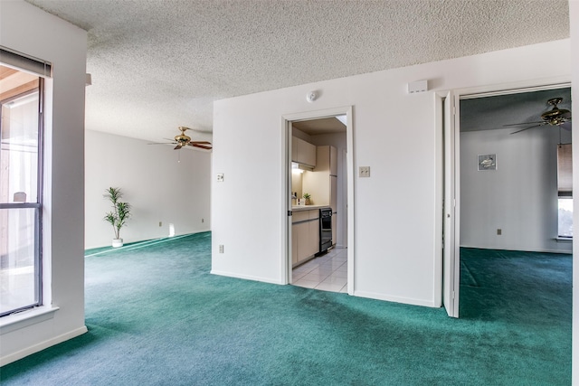 empty room featuring baseboards, light carpet, a textured ceiling, and a ceiling fan