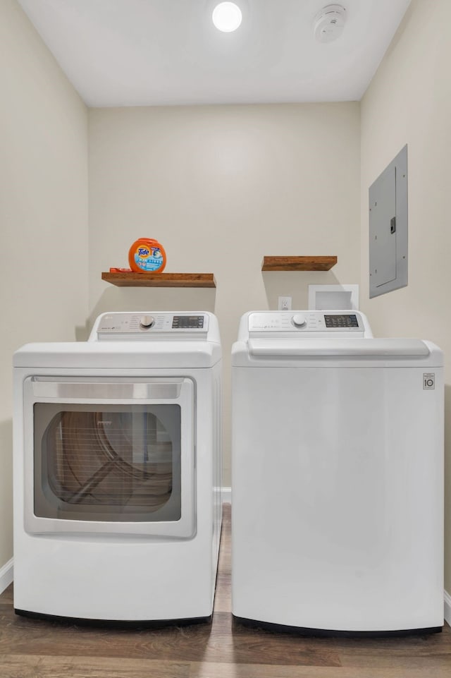 clothes washing area featuring electric panel, wood finished floors, washing machine and dryer, baseboards, and laundry area