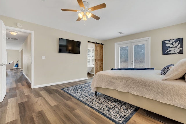 bedroom with visible vents, wood finished floors, a barn door, french doors, and baseboards