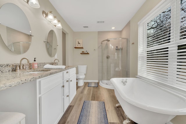 full bath featuring visible vents, a shower stall, toilet, wood finished floors, and a sink