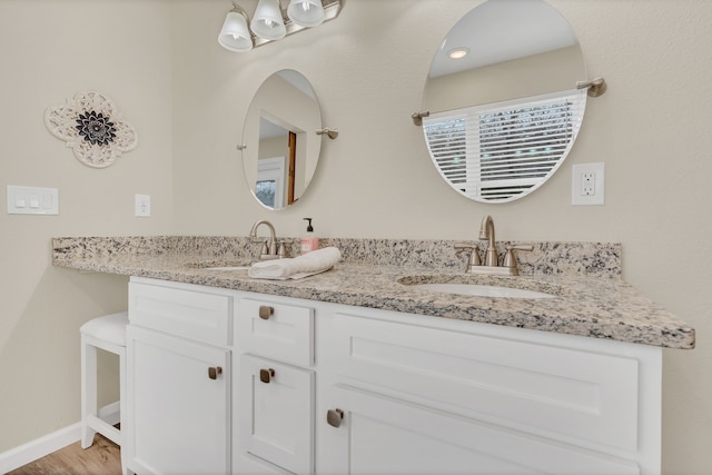 full bath featuring double vanity, wood finished floors, baseboards, and a sink