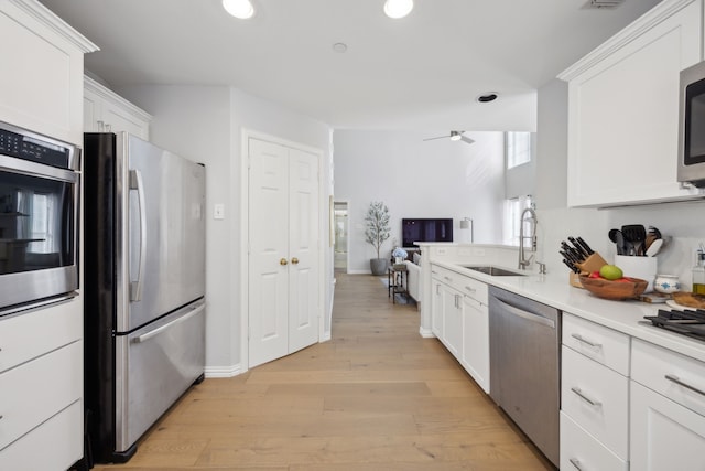 kitchen with a sink, white cabinetry, stainless steel appliances, light wood finished floors, and light countertops