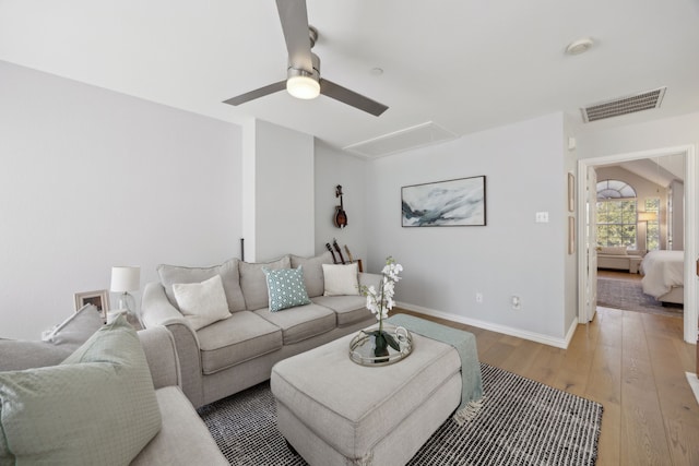 living room featuring visible vents, baseboards, attic access, light wood-type flooring, and a ceiling fan