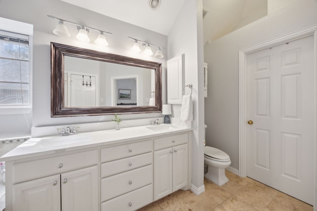 bathroom with double vanity, vaulted ceiling, toilet, and a sink