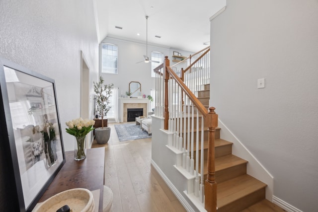 staircase featuring a fireplace, a ceiling fan, baseboards, and wood-type flooring