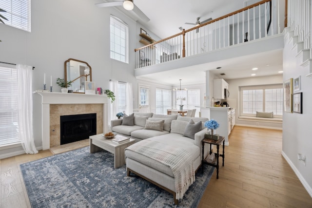 living room with a tiled fireplace, a ceiling fan, baseboards, and light wood finished floors