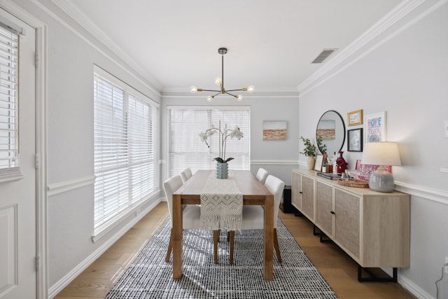 dining space featuring light wood finished floors, a notable chandelier, visible vents, and ornamental molding