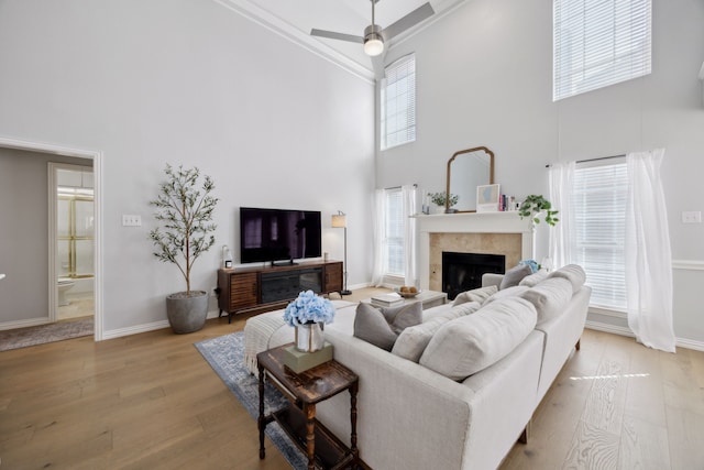 living area with a tiled fireplace, baseboards, ceiling fan, and hardwood / wood-style flooring